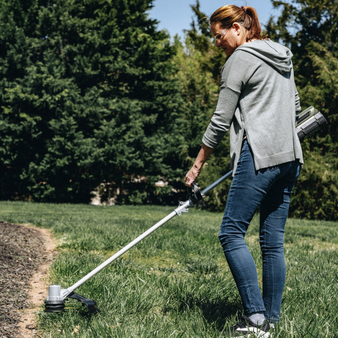 Woman using Green Machine string trimmer to trim grass.