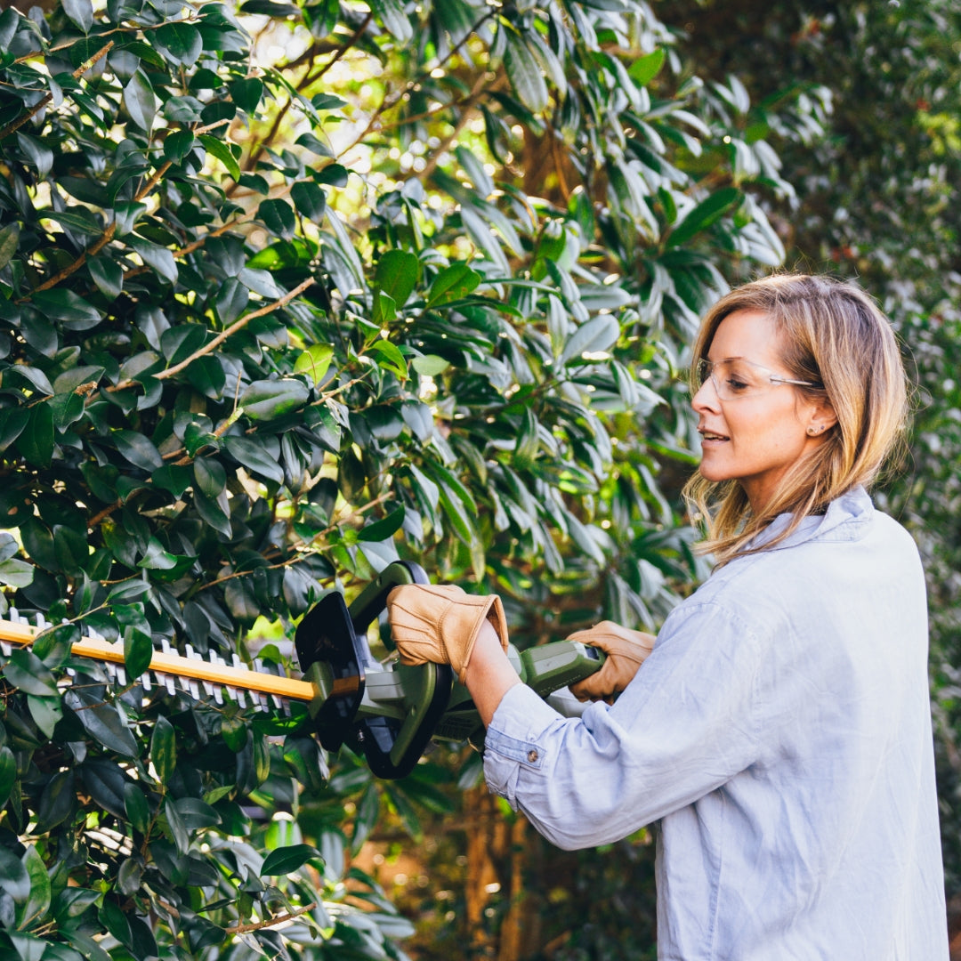 Woman using Green Machine hedge trimmer to trim hedges.